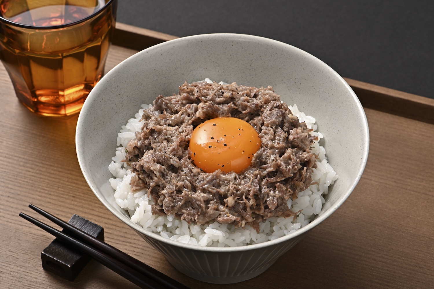 シチュエーションの撮影実績：コンビーフをご飯の上に盛り付け、中央に卵黄を添えた食品写真です。