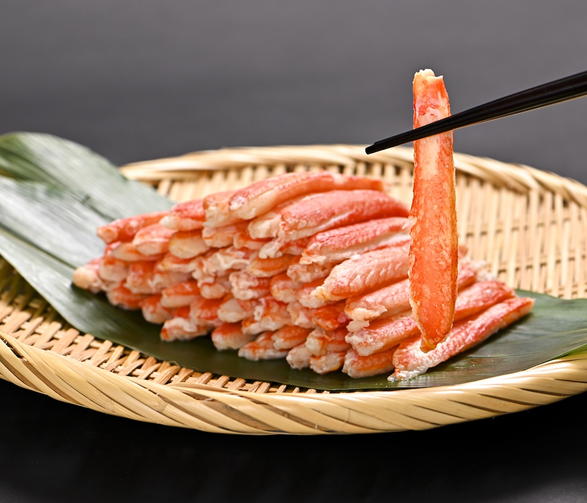 シチュエーションの撮影実績：冷凍カニの内容量と個体のサイズ感が伝わるよう、竹かごに複数を盛り付け、一本を箸で持ち上げる構成で撮影しました。