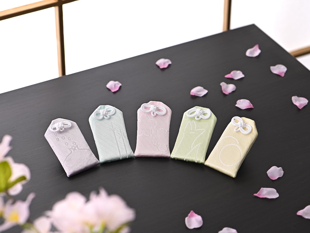シチュエーションの撮影実績：淡い紫、ブルー、ピンク、グリーン、イエローの布製小物入れを黒いテーブルに並べ、色と刺繍、上部のひもの違いが見比べやすいように撮影しました。