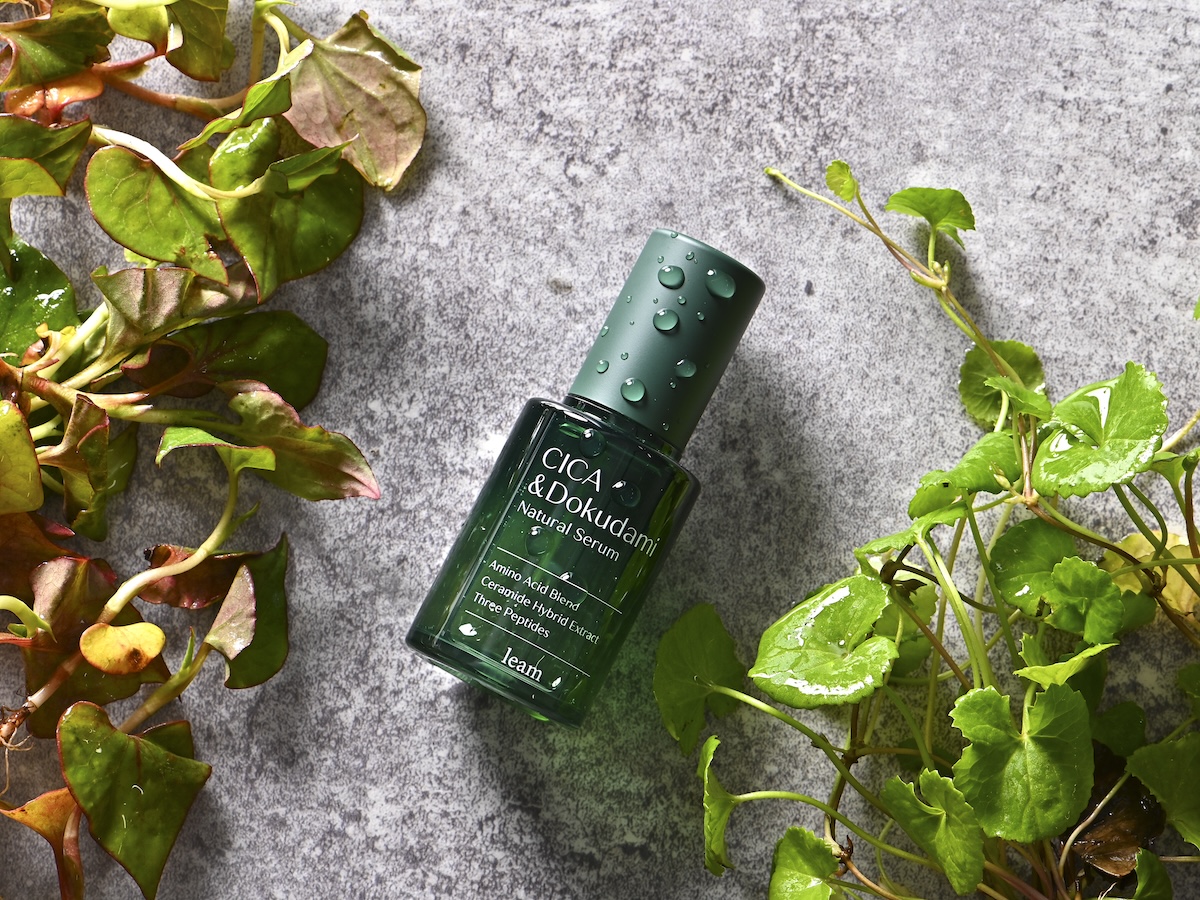 シチュエーションの撮影実績：「CICA & DOKUDAMI Natural Serum」と書かれた深いグリーンのボトルを中央に置き、周囲に濡らしたドクダミの葉を配置して、みずみずしい印象を表現しました。