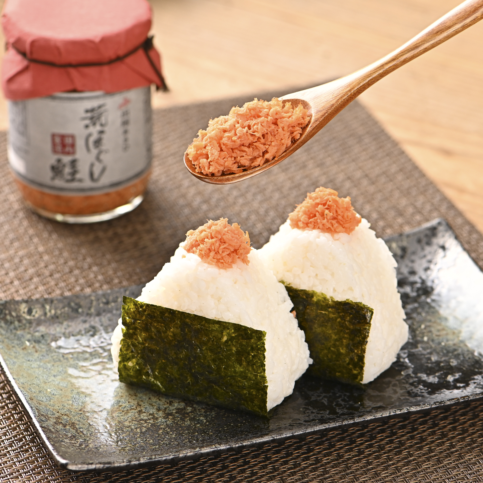 シチュエーションの撮影実績：鮭のほぐし身を木のスプーンですくい、手前のおにぎりに添えた状態と瓶入りの商品を一緒に撮影しました。