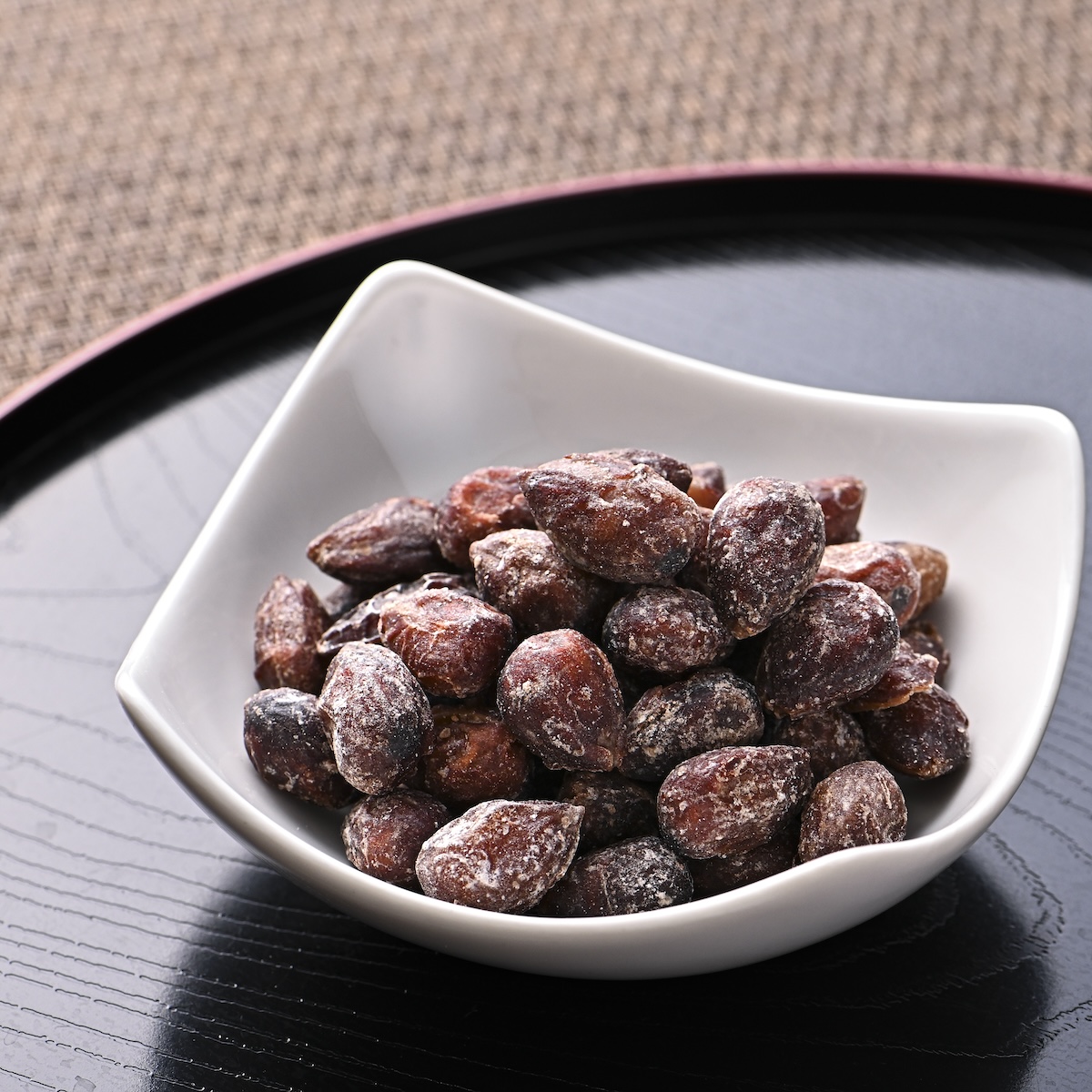 シチュエーションの撮影実績：表面に白い粉をまとった茶褐色の豆菓子を素朴な白い器に盛り、ひと粒ずつの形と表面の質感が見えるように撮影しました。