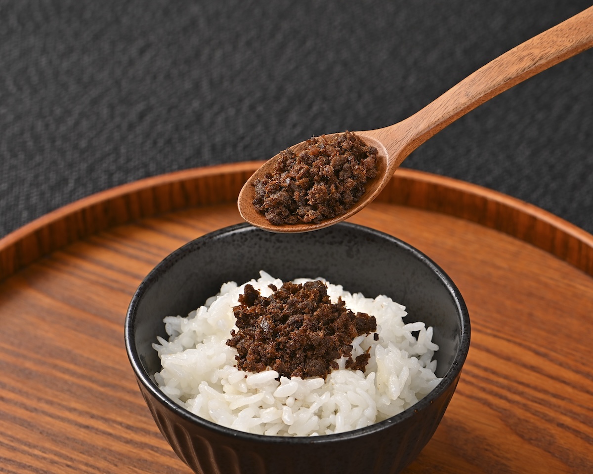 シチュエーションの撮影実績：白いご飯を黒い器に盛り、濃い色の具材を中央にのせ、木のスプーンですくった状態を上方に配置して撮影しました。